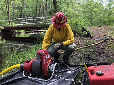 wildland firefighter works with a pump to bring water to a wildfire